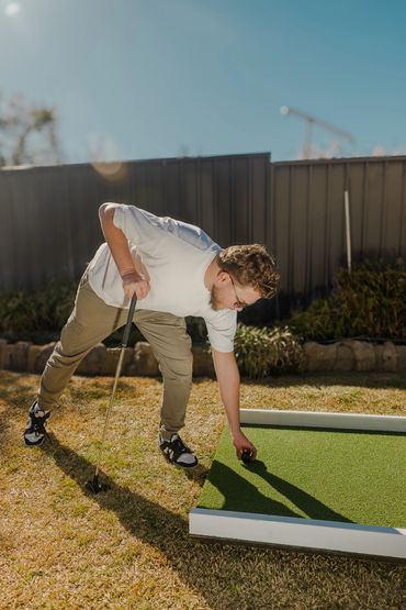 Man playing mini golf outdoors on a sunny day.
