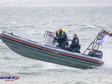 Three people riding a Gemini inflatable boat at high speed on choppy water.
