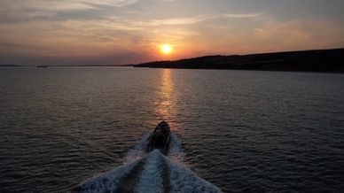 Boat cruising on water at sunset with sun low on horizon.