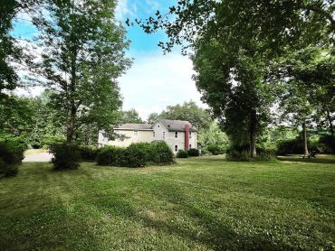 Large green lawn with trees and a white house.