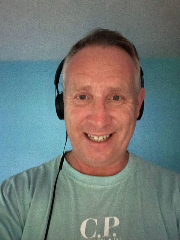 Smiling man wearing headphones and a light blue C.P. Company t-shirt.