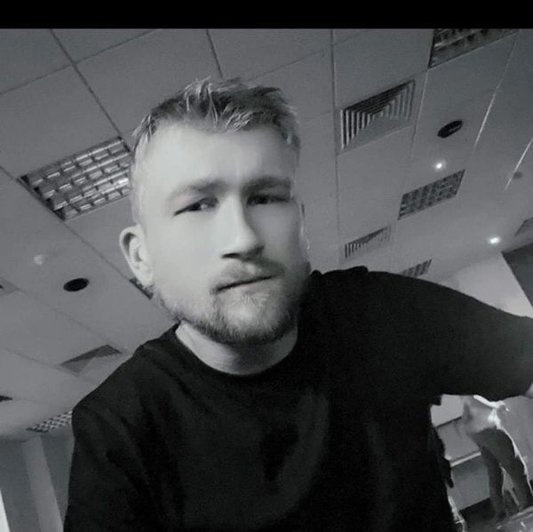 Black and white selfie of a man with a beard in an indoor setting.