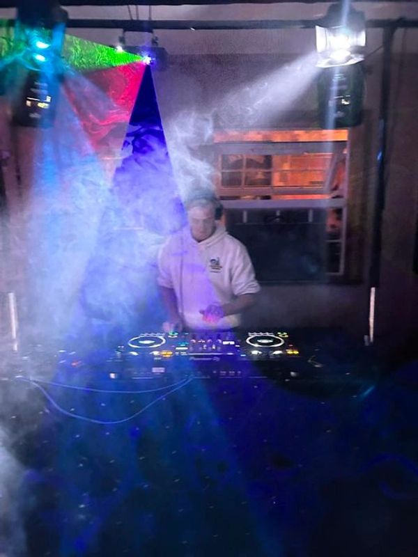DJ performing with colorful lights and smoke effects in a dimly lit room.