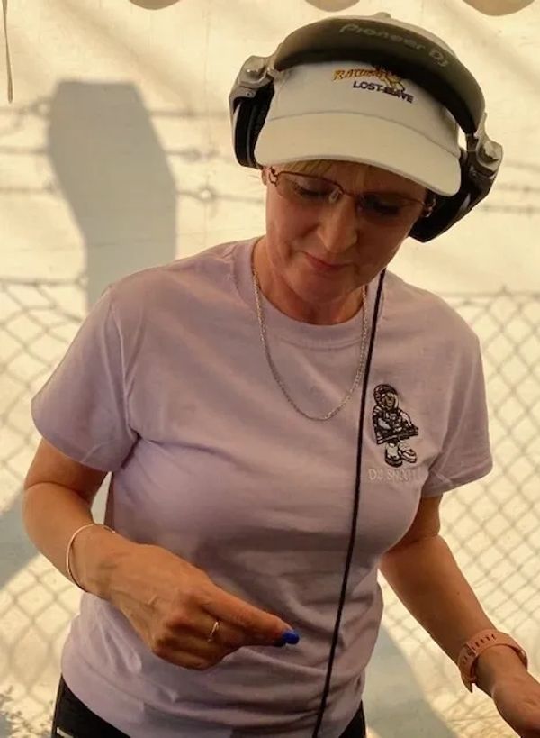 A woman DJ wearing headphones, glasses, and a cap, adjusting music equipment.