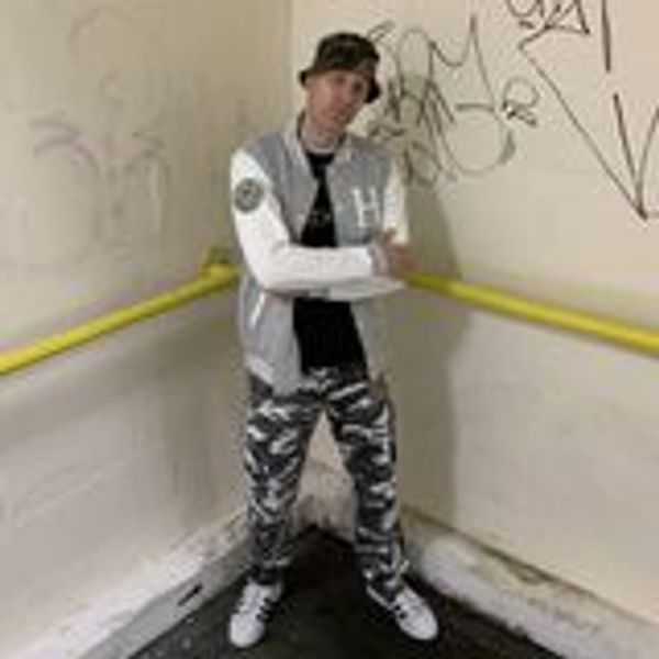 A young man in casual streetwear stands confidently in a graffiti-covered stairwell.
