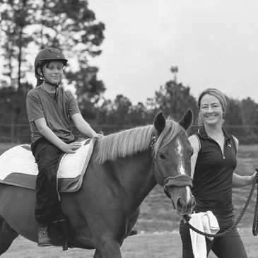 A child on horseback with an adult holding the reins, smiling.