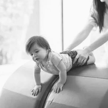 A baby crawling with adult support on a padded surface.