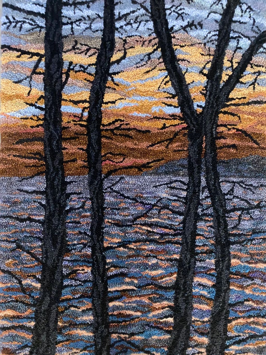 Hand hooked rug of tree trunks along the East Coast Trail, Newfoundland, against a colorful sunset sky.