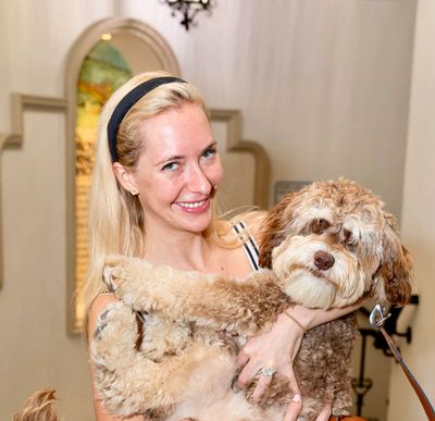 Smiling woman holding a fluffy brown and white dog indoors.