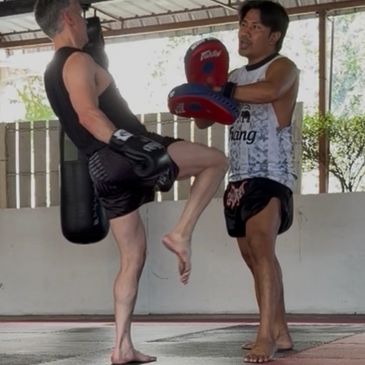 Two men practicing Muay Thai with kick pads in a gym.
