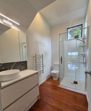 Completed bathroom renovation in Maungakaramea with a white vanity, glass shower and timber floors