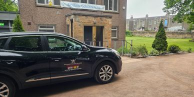 Black SUV parked near a brick building with a banner.