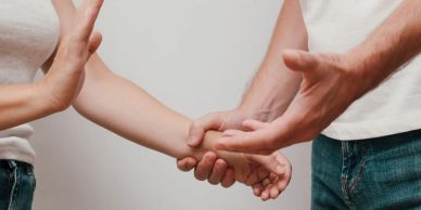 Two people holding hands while a third person pushes away.