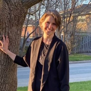 Smiling woman leaning on tree outdoors in sunlight.