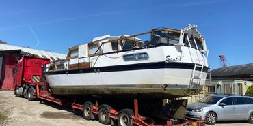 White boat named Santel on a red trailer with a red truck and a silver car nearby.
