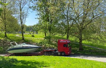 A red truck transports a boat on a sunny day with green trees and grass.
Daf XF 105 with boat traile
