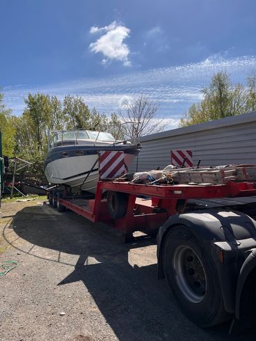 Boat being transported on a red trailer under a blue sky.