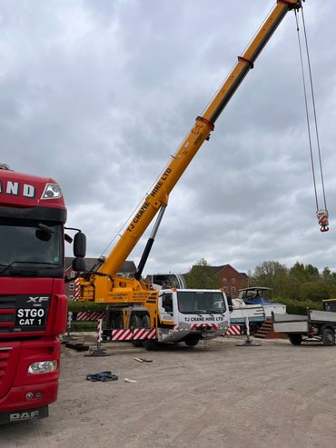 Yellow TJ Crane Hire Ltd crane lifting equipment at a construction site with a red truck nearby.