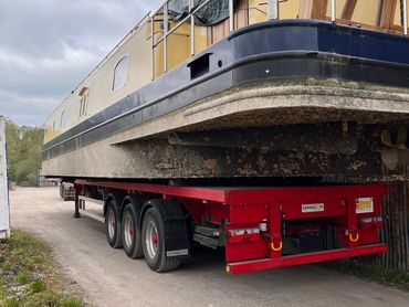 A long narrow boat on a red trailer under a cloudy sky.