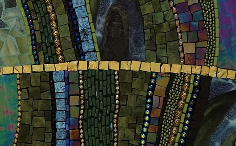 A close up of a mosaic art piece made with green glass and beads. 