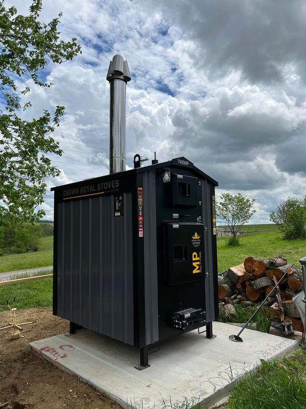 A black Crown Royal wood stove with a chimney outside on a concrete slab.