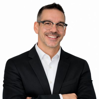 Smiling man in black suit and glasses posing confidently.