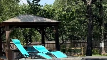 A backyard with a dual-level pool and turquoise lounge chairs under a wooden gazebo.