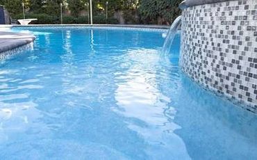 Clear blue water flowing into a swimming pool with a tiled edge.
