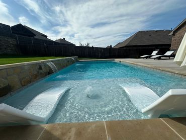 Modern backyard pool with water features and lounge chairs.