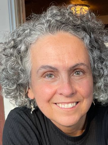 Smiling woman with curly gray hair wearing a black top and earrings.