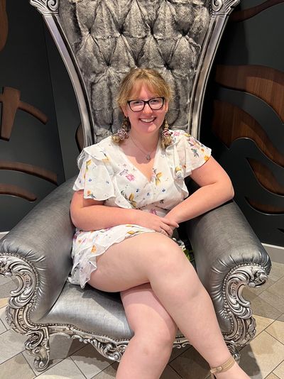 Smiling woman in floral dress sits on an ornate silver chair.