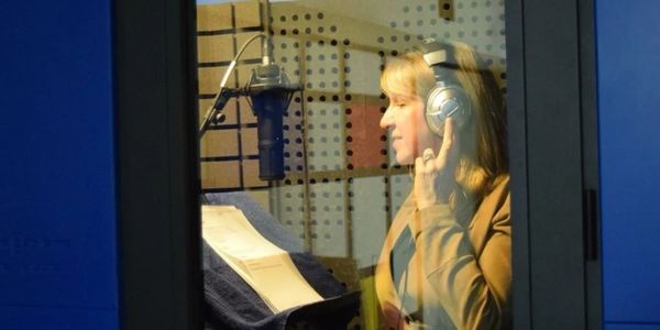 Woman recording audio in a professional studio booth wearing headphones.