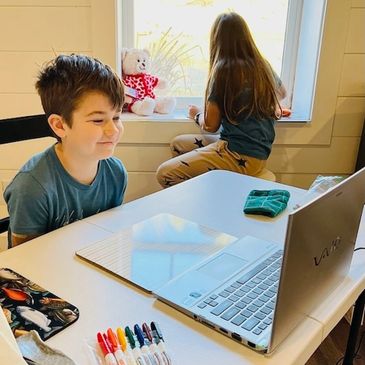 A boy sitting in front of a laptop and a girl sitting behind him with her back turned to him