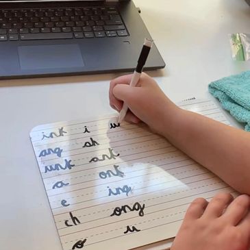 A child's hands writing combinations of letters in cursive on a dry erase board