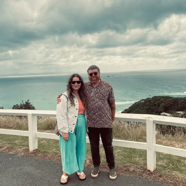 A man and woman posing by a seaside viewpoint with cloudy skies.