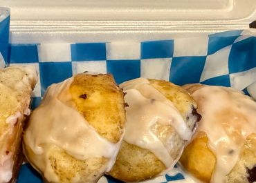 Four glazed cinnamon rolls in a takeout container with blue checkered paper.