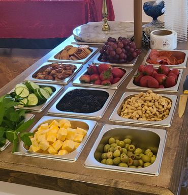 A wooden table with metal trays filled with various snacks and fruits.
