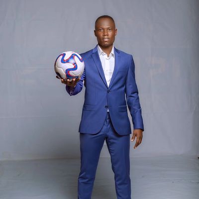 Man in blue suit holding a soccer ball confidently.