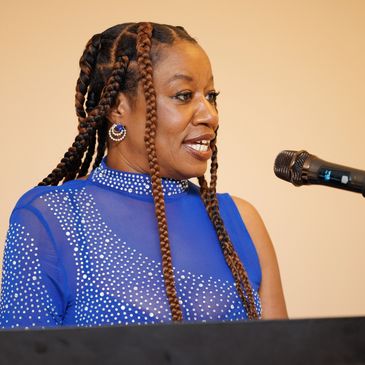 Woman speaking at a microphone in a blue dress.