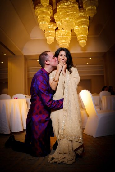 A man kisses a woman on the cheek in a warmly lit elegant setting.