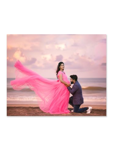 Couple's beach maternity photoshoot with flowing pink dress and romantic pose.