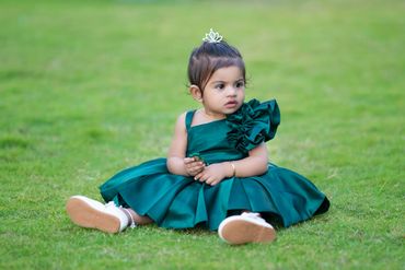 Adorable toddler in a green dress sitting on grass, looking curious.