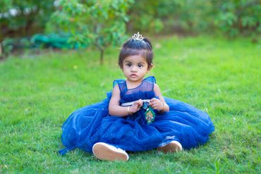 A toddler girl in a blue dress sitting on grass.
