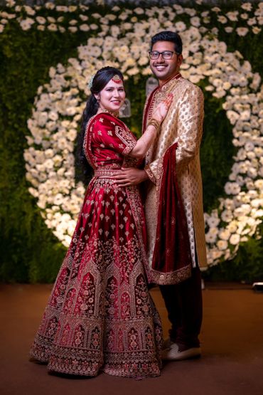 A couple in traditional Indian attire posing in front of a floral backdrop.