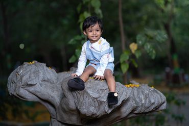 A happy toddler sitting on a large stone sculpture outdoors.