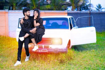 Young couple in black outfits posing affectionately by a vintage white car with open doors.