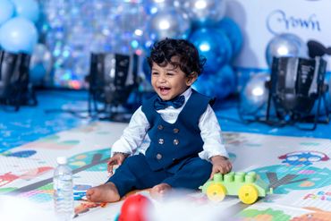 Happy toddler in a blue suit playing with a green toy car.