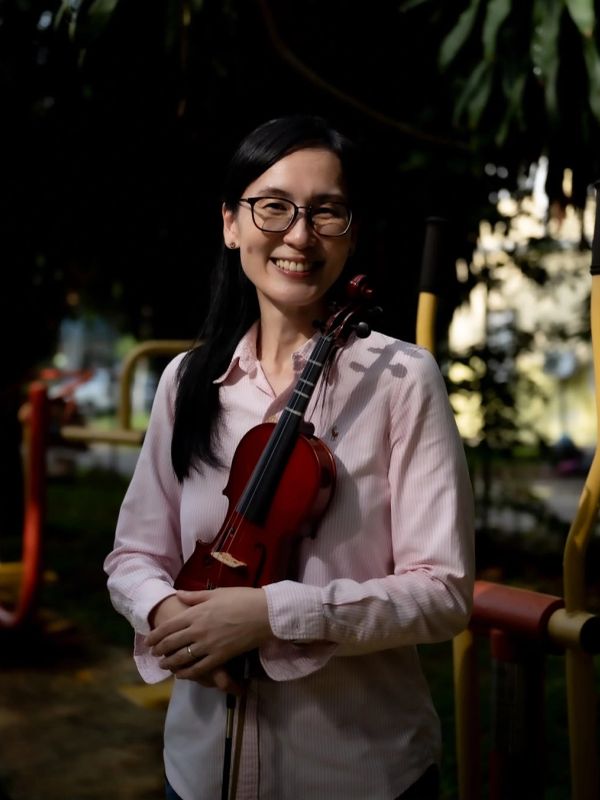 Woman smiling and holding a violin outdoors.