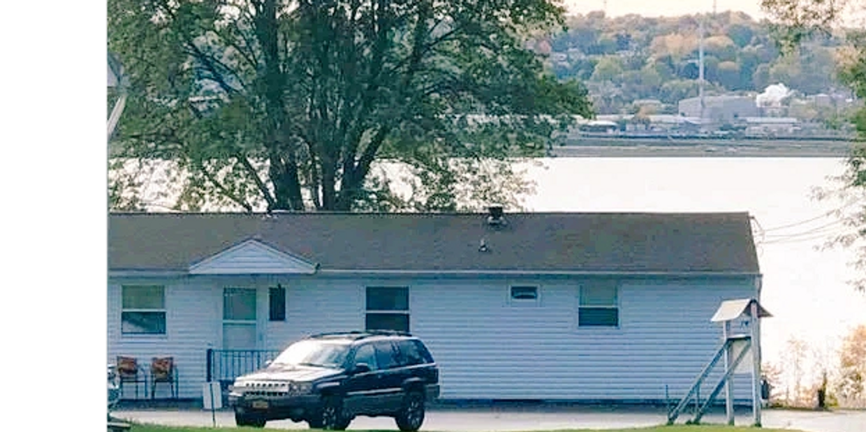 A black SUV parked in front of a single-story house near a body of water.