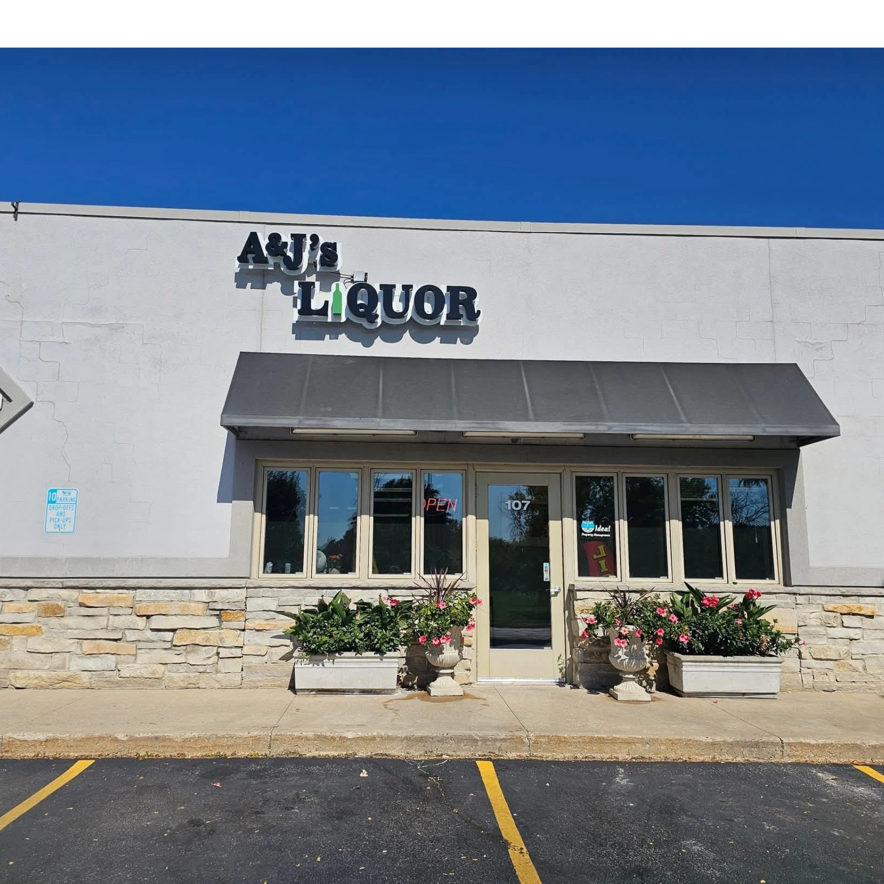 Front view of A&J's Liquor store with a black awning and flower pots.